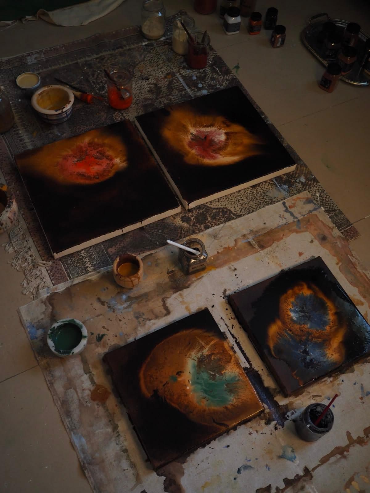 Cuatro obras de Carla Kasseroler en el suelo del taller, con formas en azul y naranja sobre fondo oscuro.