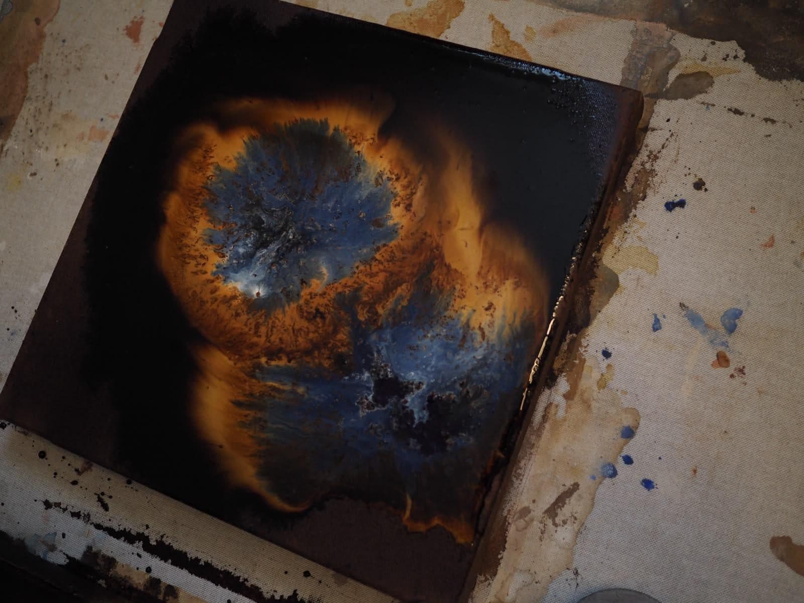 Obra de Carla Kasseroler en el suelo del taller: una forma orgánica en azules y naranjas sobre fondo oscuro.