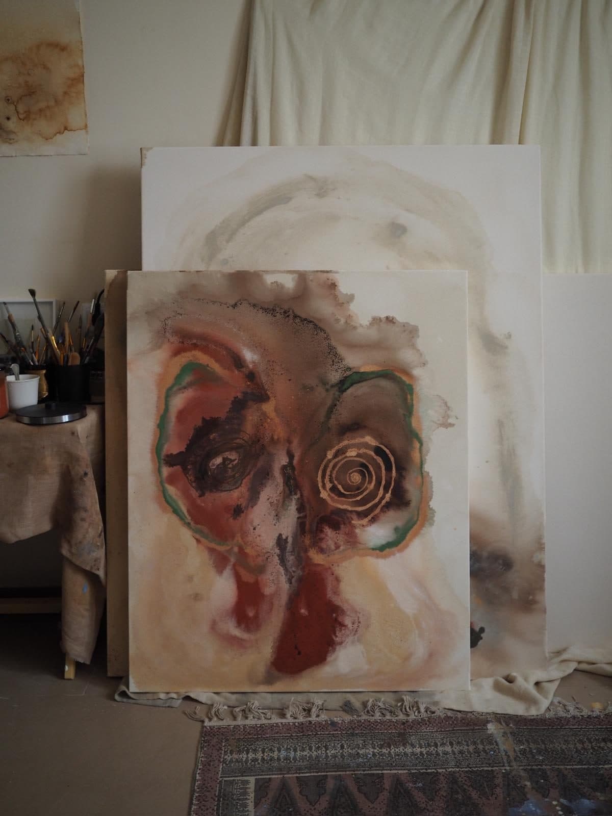 Obra de Carla Kasseroler con una forma orgánica en rojos y verdes, apoyada entre otros lienzos en el taller.