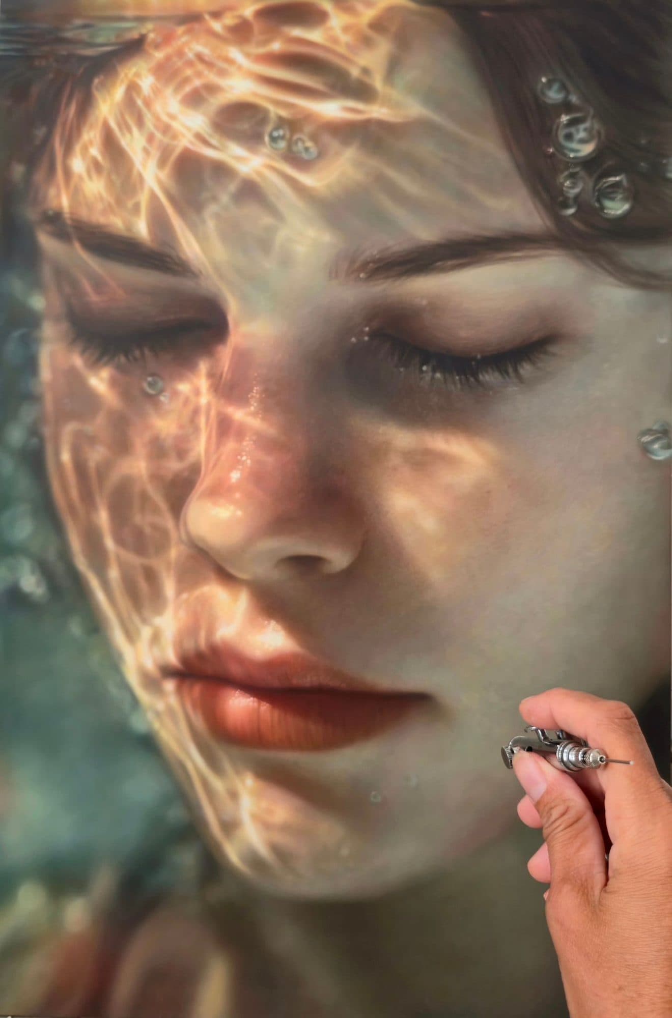 Detalle de una obra hiperrealista de Marissa Oosterlee: un rostro bajo los reflejos del agua, con la mano de la artista pintando.