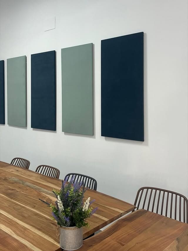Sala de reuniones con cuatro paneles verticales en verde salvia y azul marino sobre la mesa de trabajo.