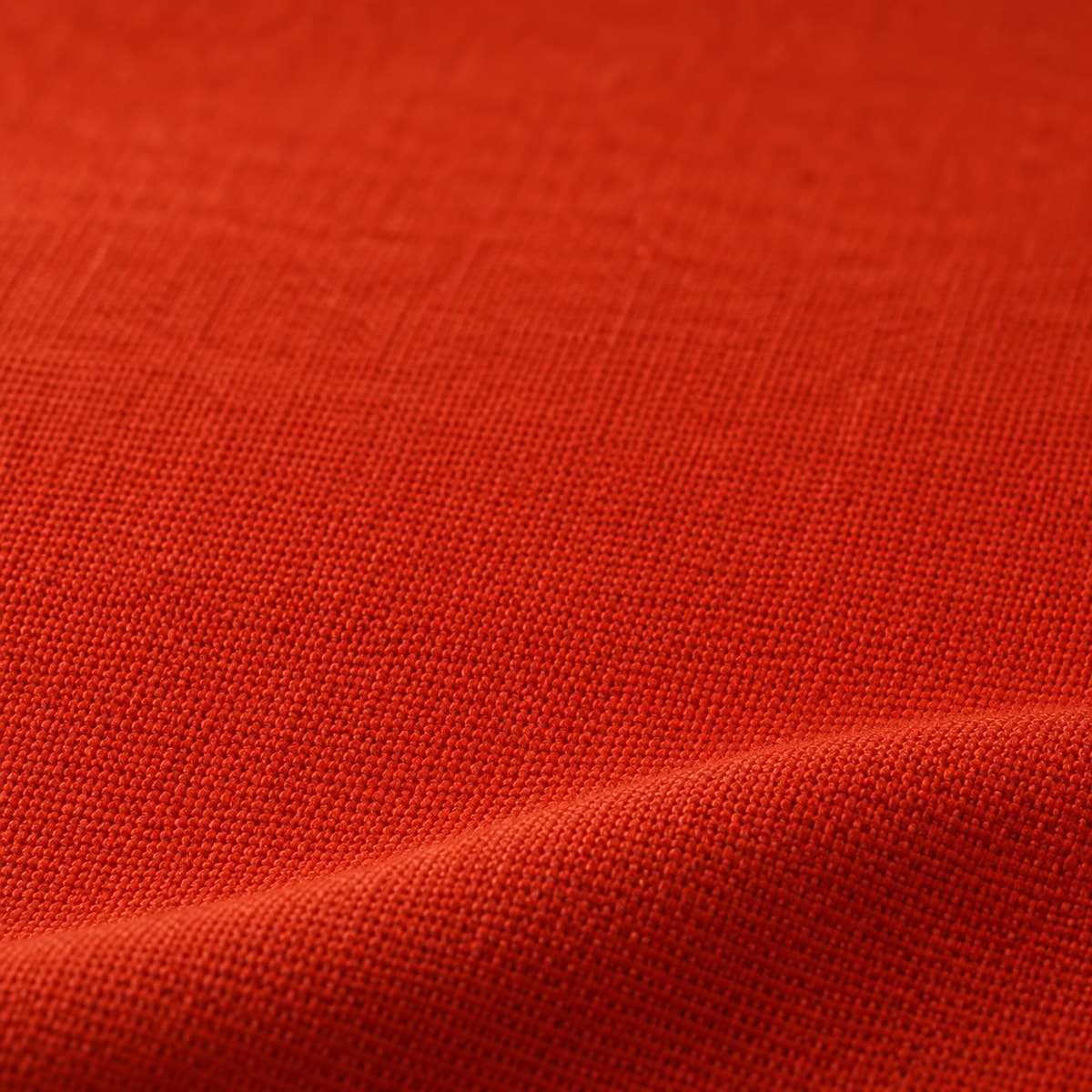 Macro de tela de algodón en terracota, un rojo ladrillo intenso de tafetán tupido y mate, con un pliegue suave y luz rasante.