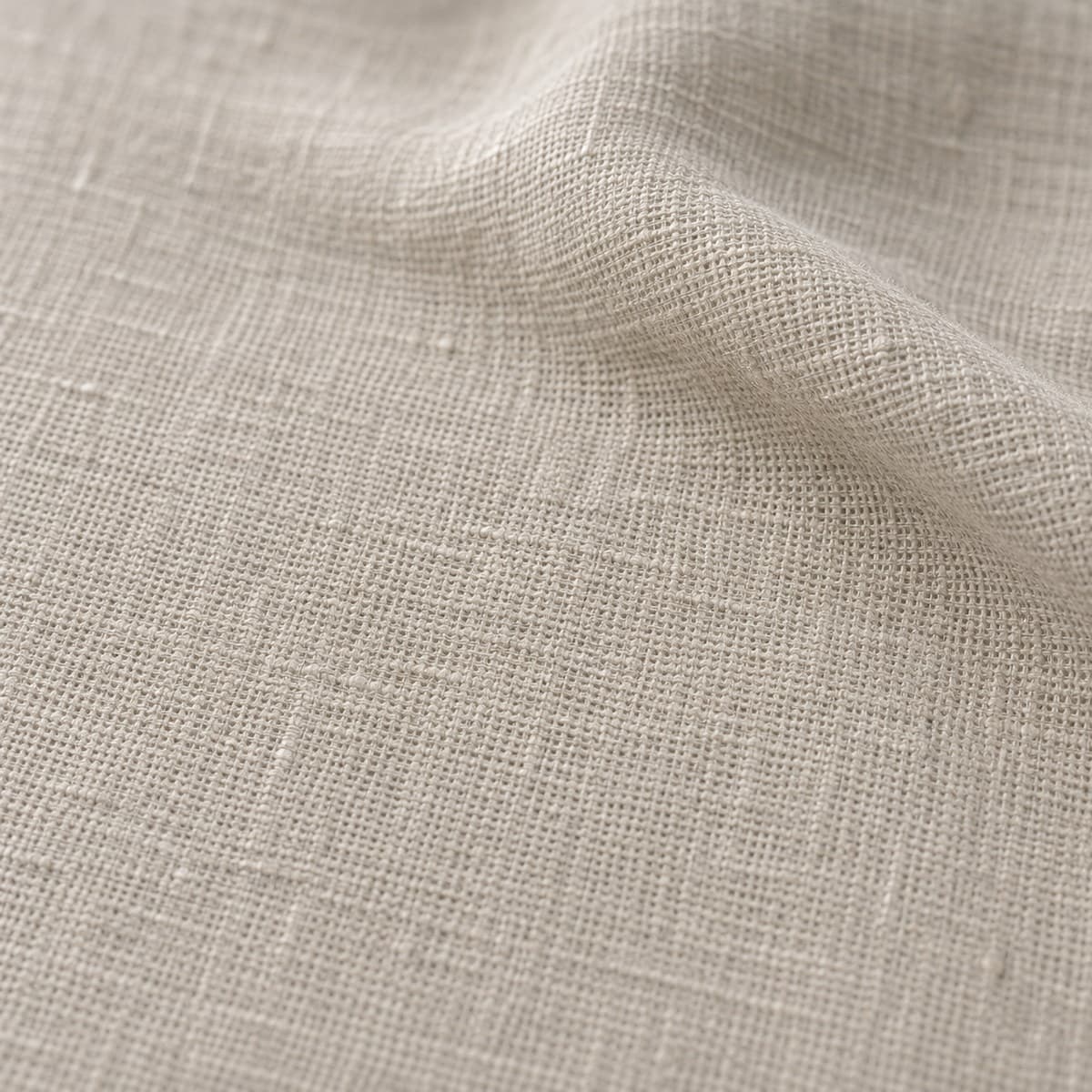 Macro de tela de lino natural, referencia 16, gris beige de poro abierto con hilos irregulares, con un pliegue suave y luz rasante.